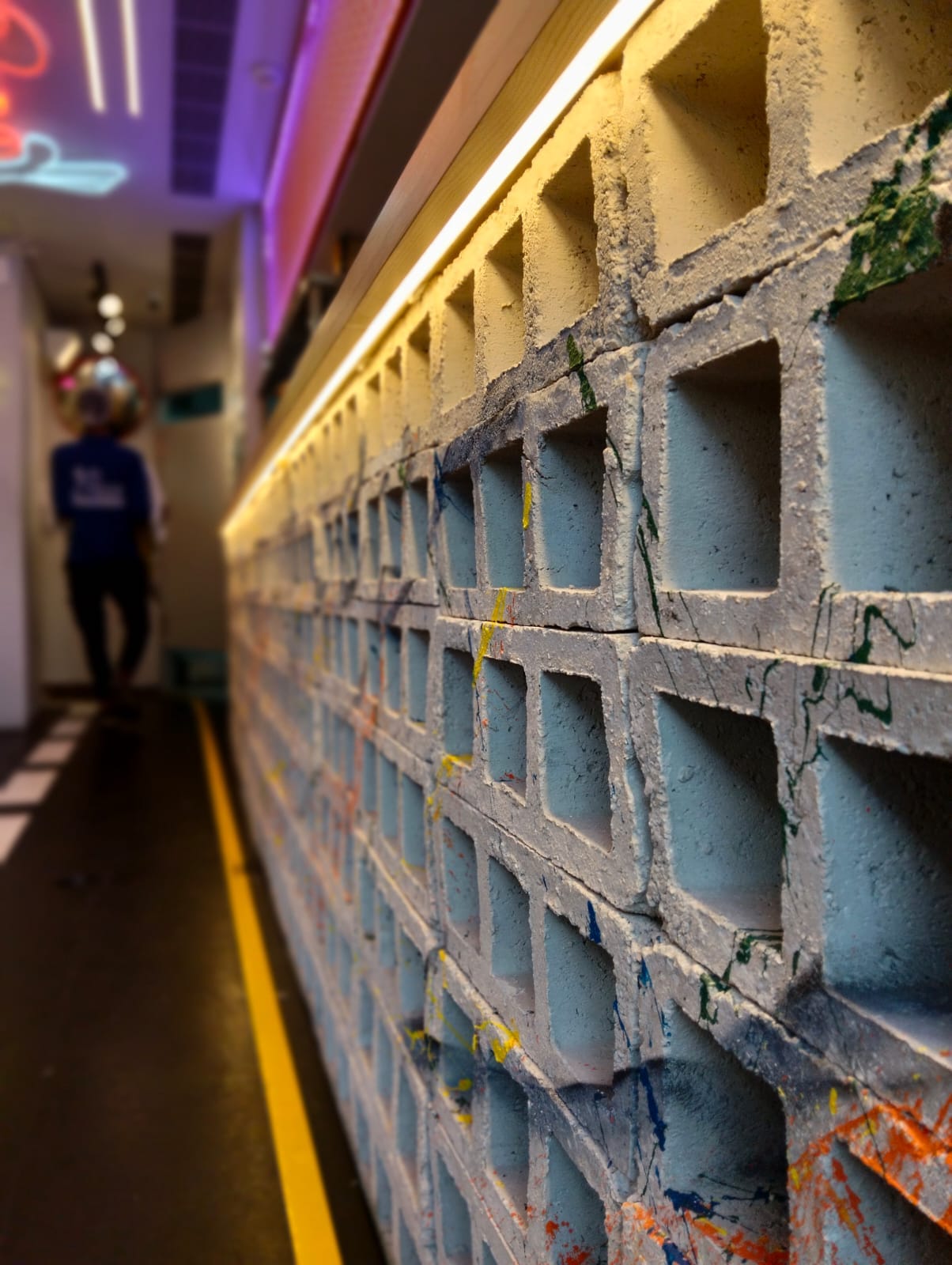 Paint-splattered hollow-block counter wall lit by a warm linear strip