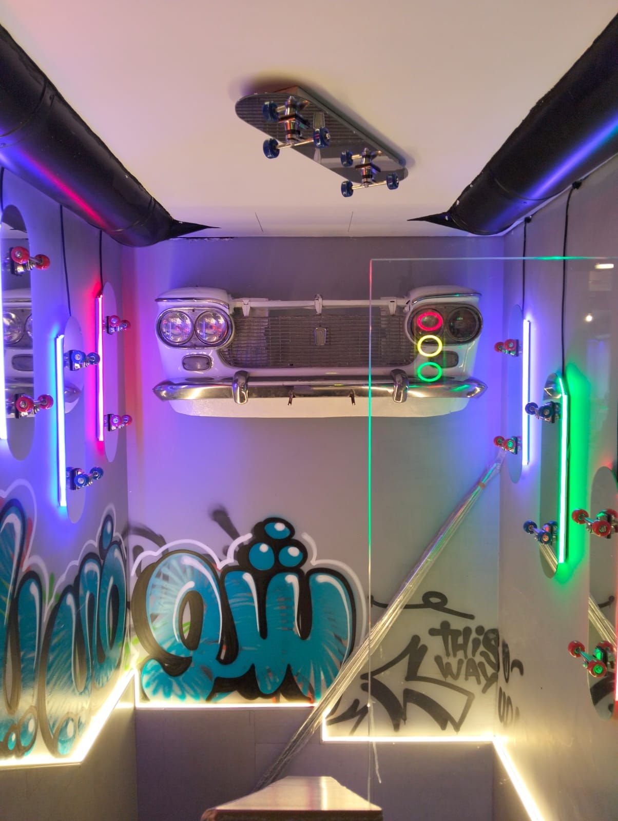 Stairwell with mounted skate decks, neon tubes and a vintage car front
