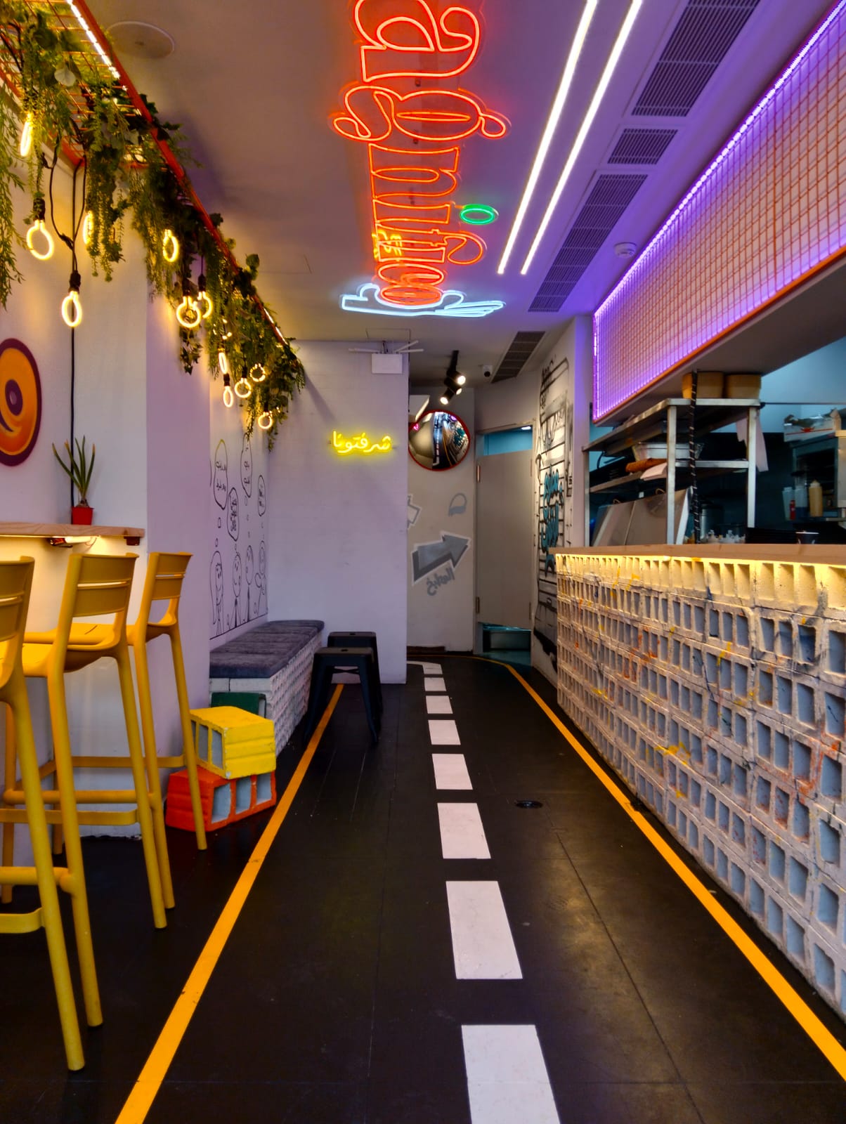 Fast food restaurant interior with Arabic neon signage, hollow-block counter and yellow bar stools