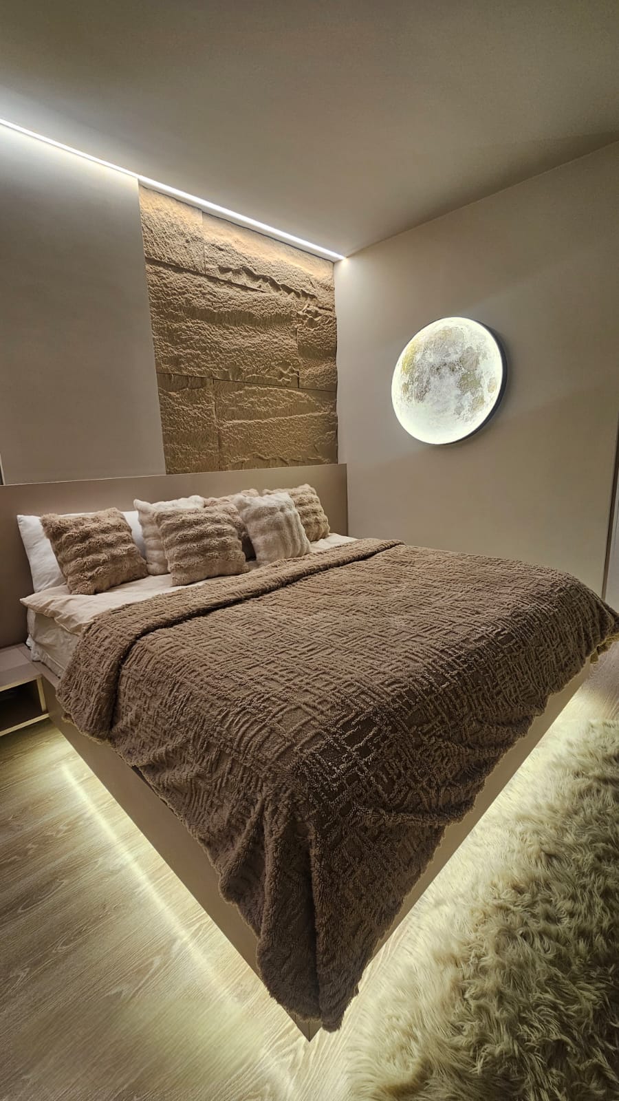 Bedroom with textured stone headboard wall and concealed lighting
