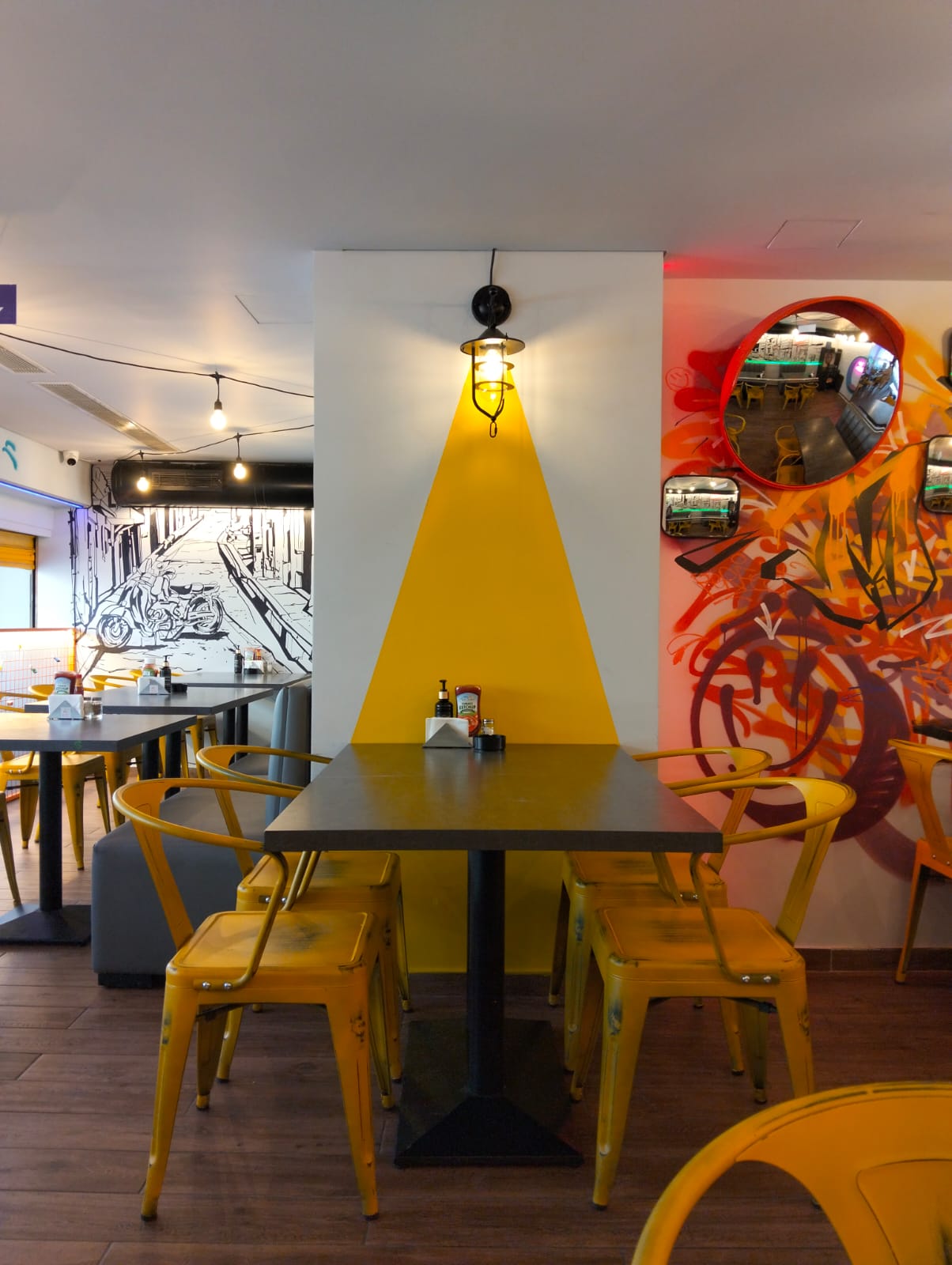 Dining area with yellow metal chairs, graffiti wall and convex mirrors