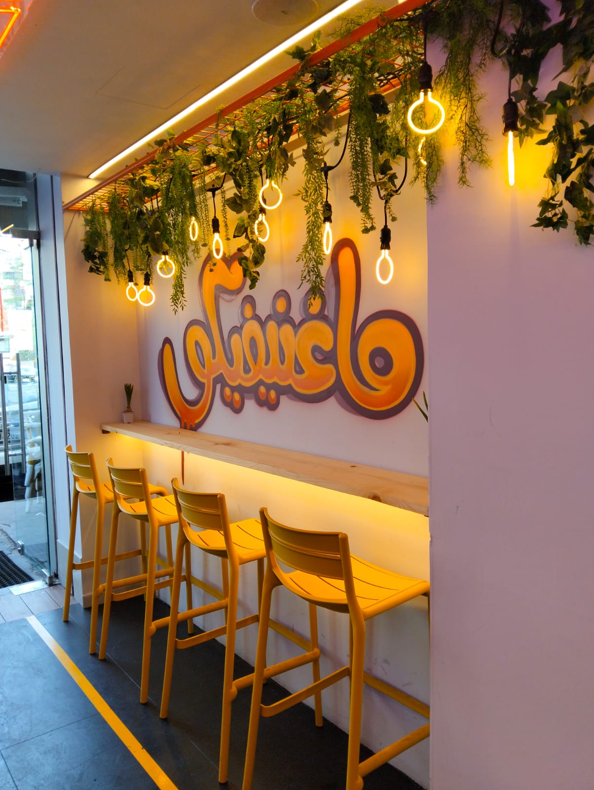 Pine bar counter with yellow stools under hanging greenery and filament rings