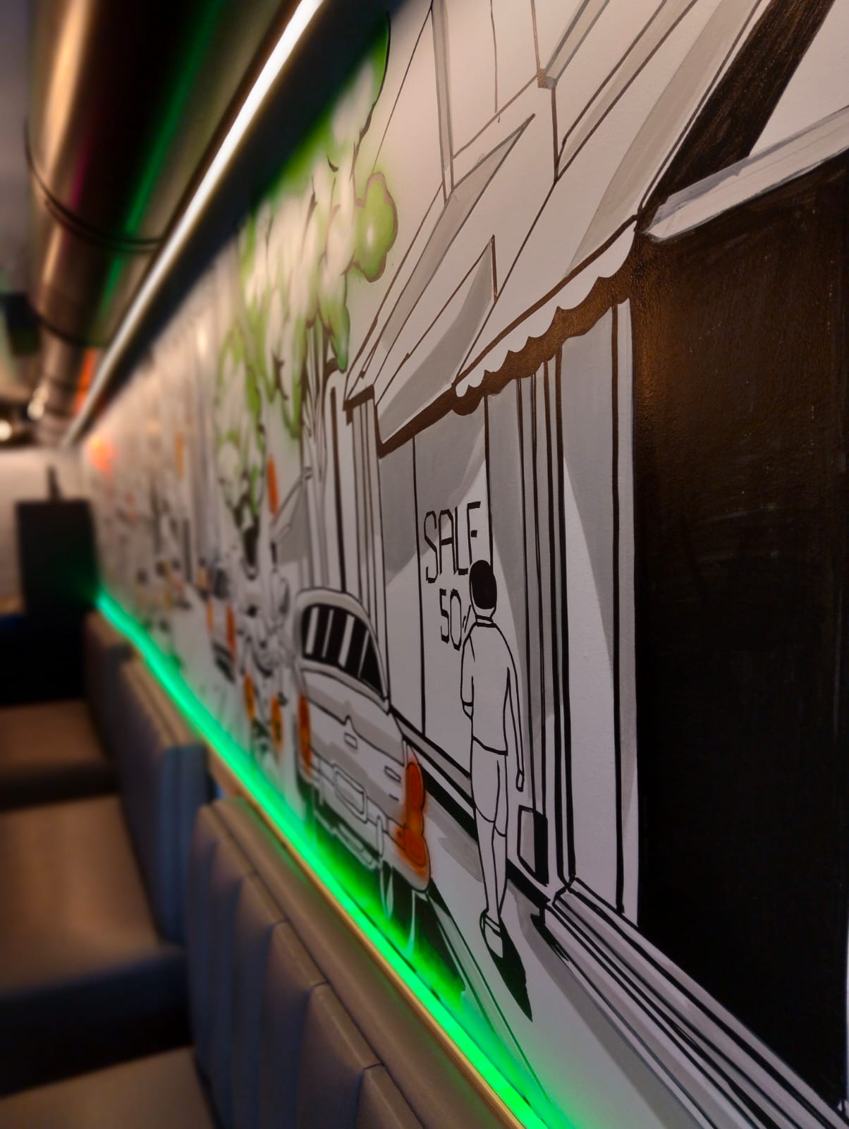 Hand-painted street mural above banquette seating with green neon trim