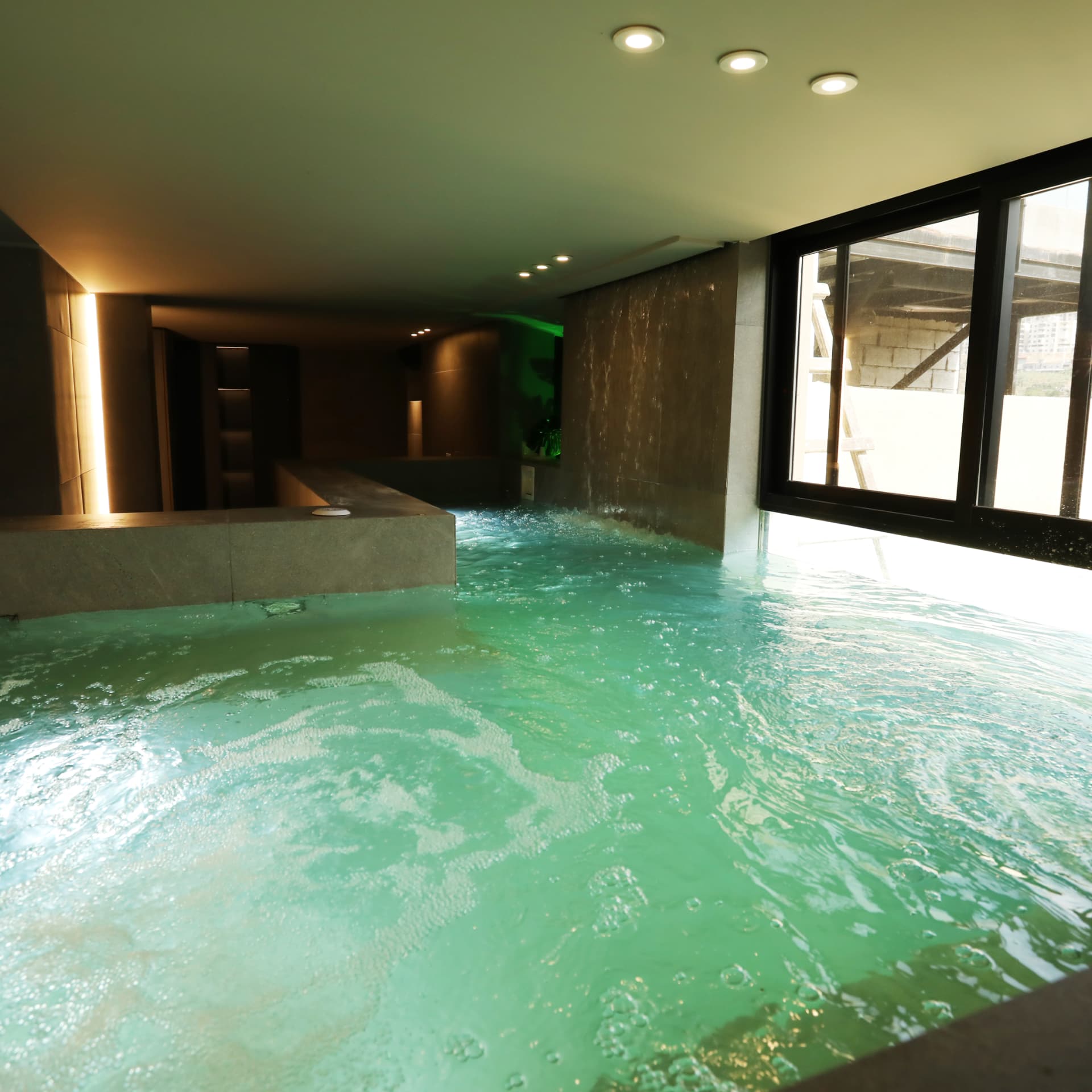 Indoor pool with water feature wall and daylight from full-height windows